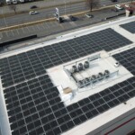Aerial view of the storage facility that shows the building with the indoor units and offices, the parking lot, and surroundin roadways. On the rood of the building is covered in solar panels